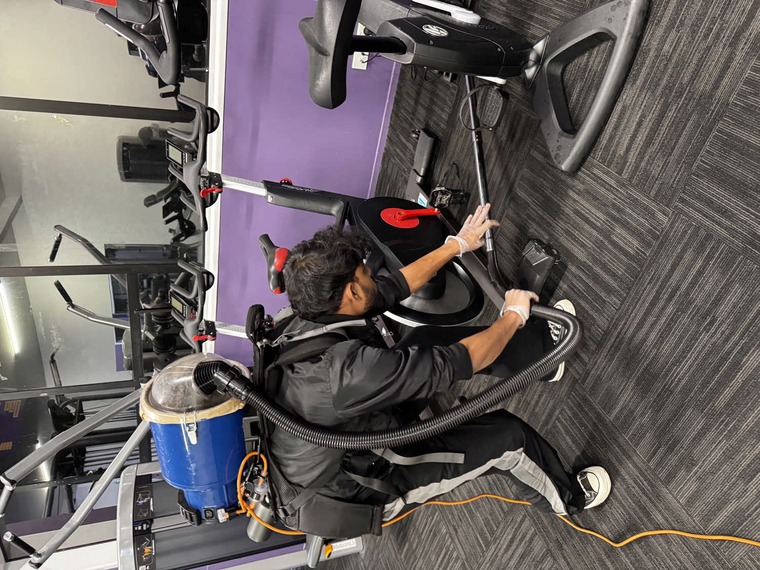 UrbanShine cleaner reaching around gym equipment during detailed commercial cleaning at a real Auckland site